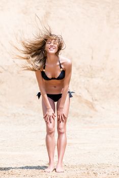 active and beautiful woman on a sand quarry in a bikini posing