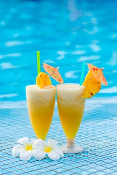 two glasses of cocktail beautifully decorated with pineapple and flowers on the edge of the pool