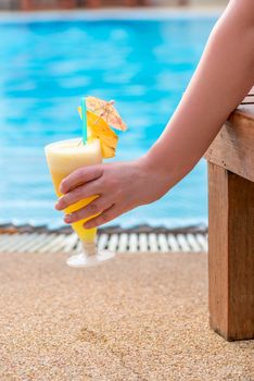 female hand holding a cocktail, picture on the background of the pool