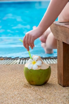 in the center of the frame is a coconut, which stands near a woman sitting near the pool