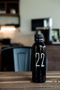 The number 22 written on a black bottle sitting on a wooden cafe table.