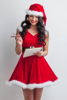 Pretty smiling pin-up Santa girl in red dress with wish list and pencil