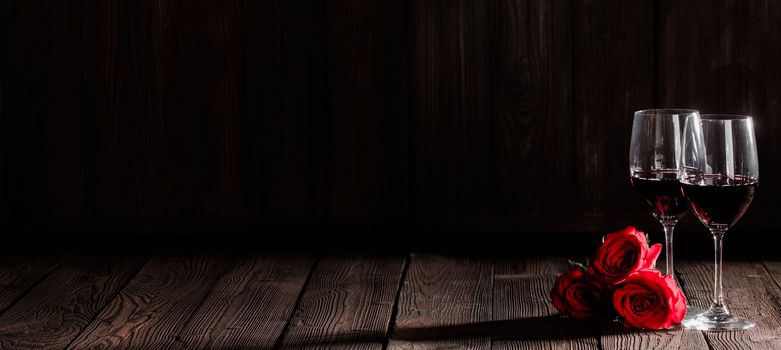 Two glasses of red wine and red roses on dark wooden background, Valentine day