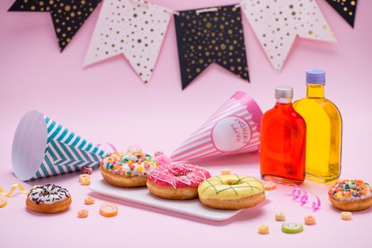 Party. Colourful round glazed donuts and bottles of drinks on pink background.