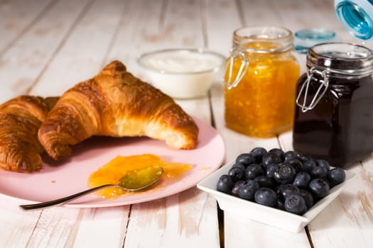 Breakfast with croissant, blueberries, yogurt and jam over a wooden table