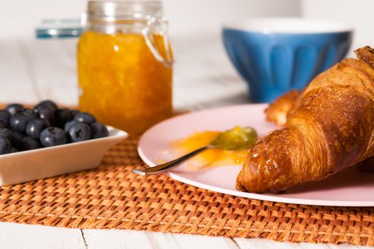 Closeup of croissant, blueberries, milk and orange jam over a tablecloth