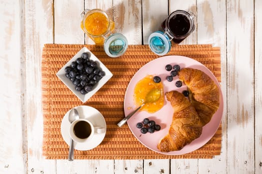 Breakfast with croissant, blueberries, coffee, orange and blueberry jam over a tablecloth seen from above