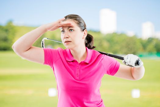woman in pink T-shirt with a golf club looks into the distance on a background of golf courses