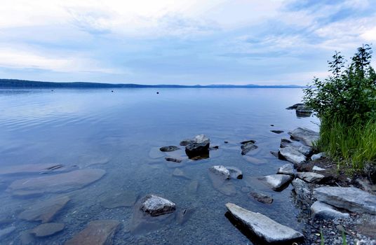 quiet lake Uvildy early in the morning, clear water, clear bottom, South Ural, in the distance are seen the Ural mountains