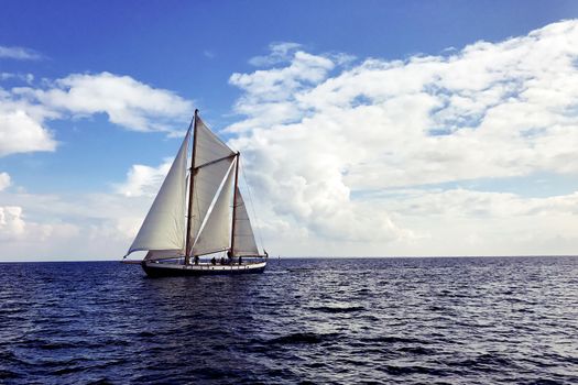 Vintage sail boat sailing on dark blue ocean under blue and cloudy sky.
