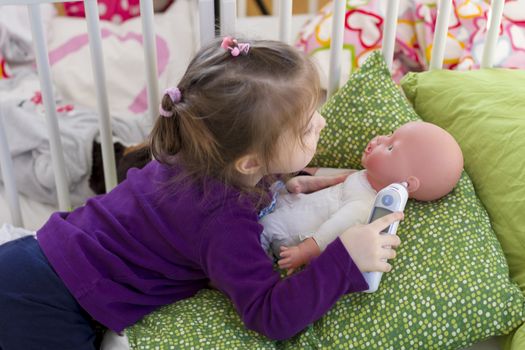 Little girl playing doctor with a doll, measuring temperature with electronic themometer and taking care of a doll, concept maternity, lifestyle and childhood