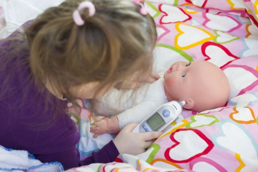 Little girl playing doctor with a doll, measuring temperature with electronic themometer and taking care of a doll, concept maternity, lifestyle and childhood