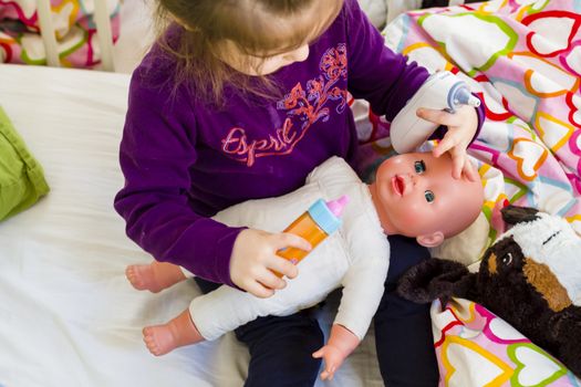 Little girl playing doctor with a doll, measuring temperature with electronic themometer and taking care of a doll, concept maternity, lifestyle and childhood