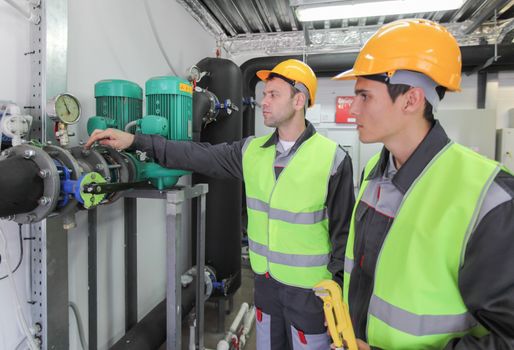 Two workers in hardhats at plant checking parameters of pressure