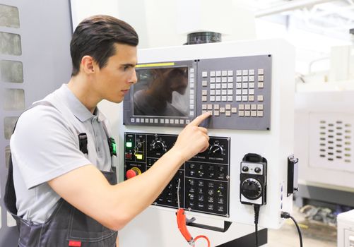 Worker pressing programming buttons on CNC machine control board in factory