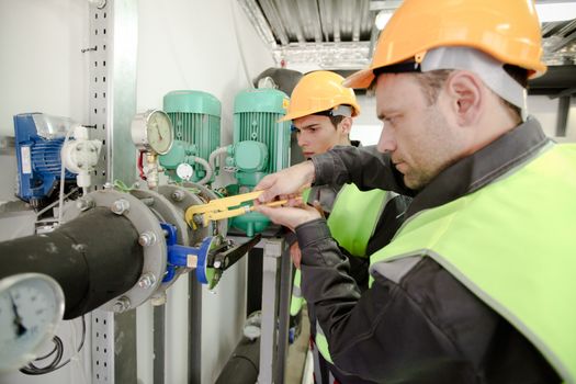 Two workers fixing pipes with manometer on high pressure system at factory