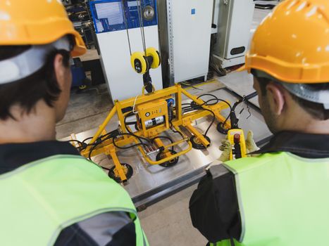 Workers near metal sheet lifting device at factory