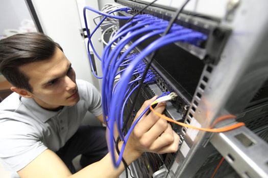 Young engeneer man in network server room connecting wires and checking rack devices