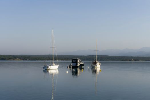 Three small boats / yachts achored in a safe bay in the morning, calm sea