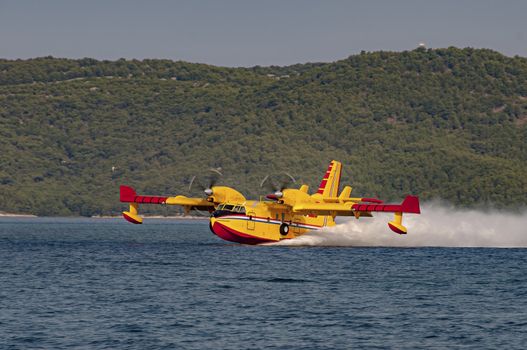 Yellow and red Canadair water bomber, turbo prop firefighting aircraft in action