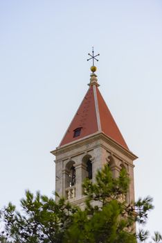Christian church steeple in front of pines on blue sky with red roof and cross on top