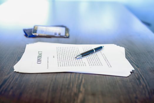 Business contract / agreement and fountain pen on dark wooden desk, with mobile phone in background, shallow depth of field, low angle