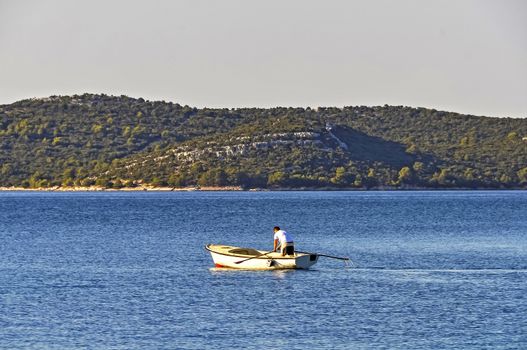 A young man practicing rowing in a traditional boat early in the morning, facing away from the viewer