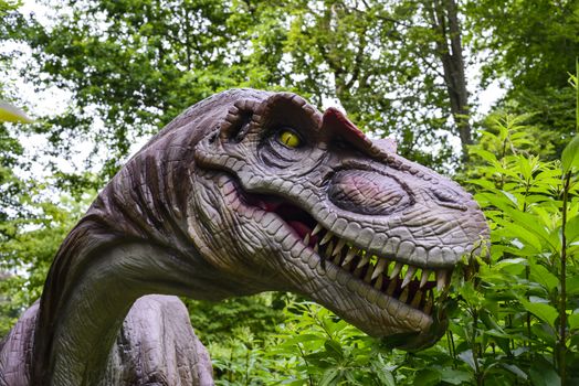 A dinosaur statue in a recreation park, greenery in background