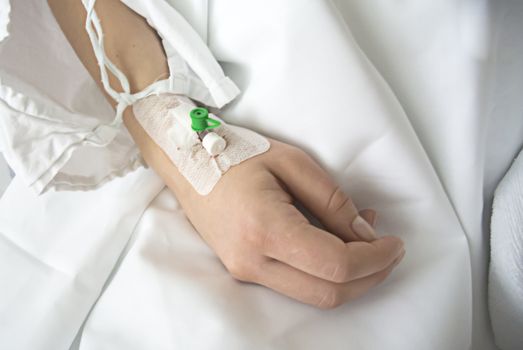 Close up of a intravenous drip in patient's hand in hospital on white sheets