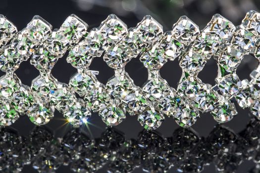 Glittery jewelry - diamond bracelet on a black background with reflections in green and blue color, dark reflective background and surface, close up macro shot