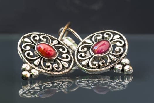 Silver earrings with red gems on dark background with beautiful reflection, close up macro shot