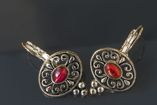 Silver earrings with red gems on dark background with beautiful reflection, close up macro shot