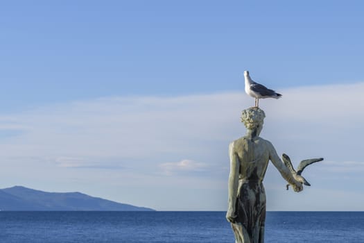 Maiden girl holding a seagull and facing the sea, statue on rocks, Opatija, Croatia