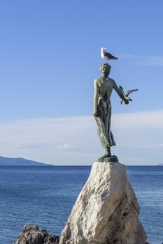 Maiden girl holding a seagull and facing the sea, statue on rocks, Opatija, Croatia