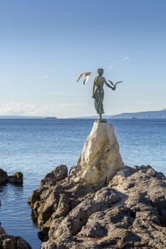 Maiden girl holding a seagull and facing the sea, statue on rocks, Opatija, Croatia