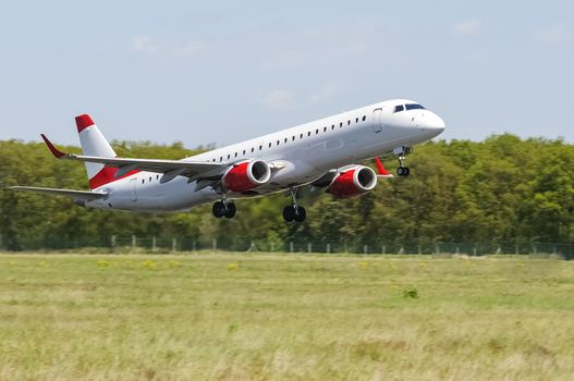 Medium sized commercial airliner with neutral livery taking off runway, twin engine, white fuselage, red stripes and engine casings