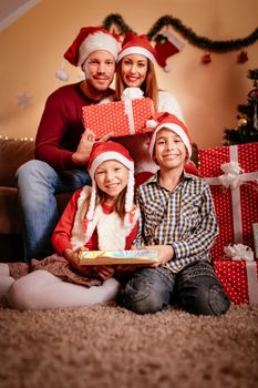 Beautiful happy family wearing santa hat and holding many Christmas gifts at home.