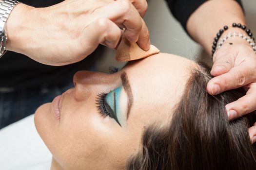 Makeup artist applying foundation using a sponge to a white woman