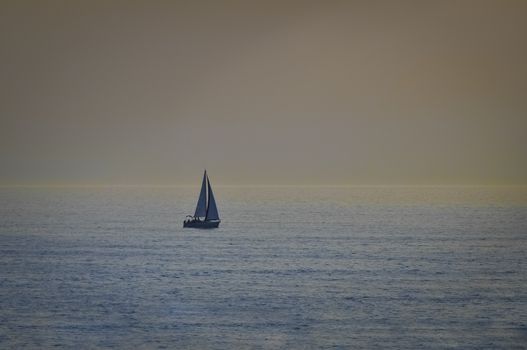 Sailboat in open sea at sunset, calm seas, no clouds