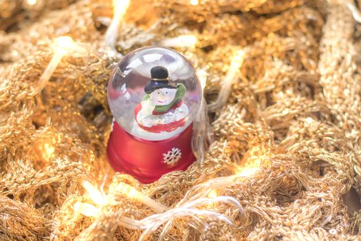 Snowman in snowglobe/snowball on golden, glittery runes with led lights illuminating the scene. Christmas home decoration example.