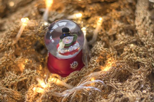 Snowman in snowglobe/snowball on golden, glittery runes with led lights illuminating the scene. Christmas home decoration example.