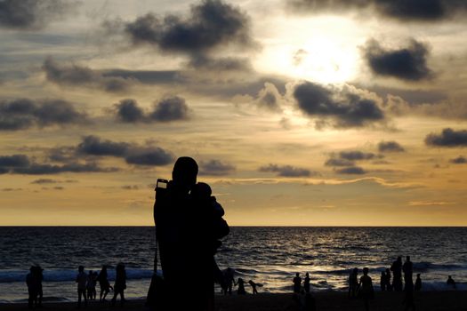 Silhouettes of woman with child and people watching a beautiful sunset on the beach of the Indian Ocean