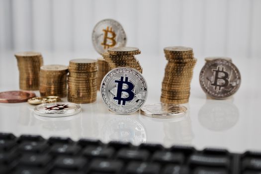 Digital currency physical silver bitcoin coin on the table near gold money and computer keyboard.