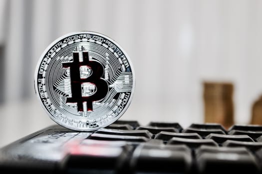 Digital currency physical silver bitcoin coin with red sign on the black computer keyboard.