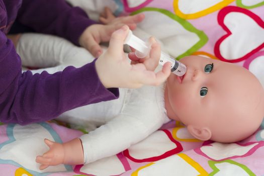 Little girl playing doctor with a doll and applying medicines with syringe and taking care of a doll, concept maternity, lifestyle and childhood