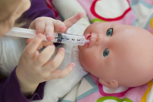 Little girl playing doctor with a doll and applying medicines with syringe and taking care of a doll, concept maternity, lifestyle and childhood