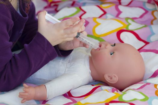 Little girl playing doctor with a doll and applying medicines with syringe and taking care of a doll, concept maternity, lifestyle and childhood