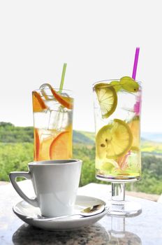 A cup of coffee and two glasses of lemonade on table, tranquil scenery in background