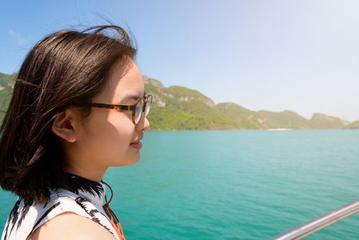 Cute young woman with eyeglasses smiling happily on the boat while cruising the natural of the sea island and under sunlight summer at Mu Ko Ang Thong National Park, Surat Thani, Thailand