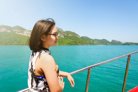 Cute young woman with eyeglasses smiling happily on the boat while cruising the natural of the sea island and under sunlight summer at Mu Ko Ang Thong National Park, Surat Thani, Thailand